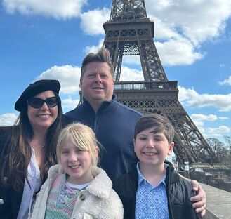 a family with 2 parents and 2 kids, the wife wears a french beret and there is the eiffel tower in the backgroud and everyone smile