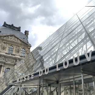 the entrance of the Louvre a tower at the left back and the pyramid front right