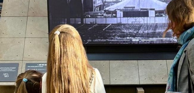 2 girls facing an archive movie with a tour guide on the right side