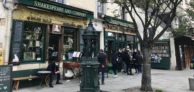 shakespear and company library in the backgroung, a yellow owning awning a wallace fontain in the front of it