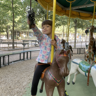 a child is having a great time on the holdest caroussel of paris made by charles garnier at the luxembourg garden on a carroussel with a jousting stick