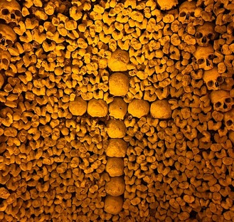 a cross made from skulls in the catacombs of Paris, the cross in against a wall of 