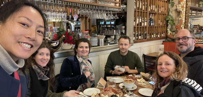 a team of happy guest is around a table enjoying the amazing dushesthat are laid out on it such as a french onion soup cheeses and cold cuts