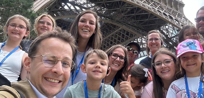 a happy family taking a tour at the eiffel tower, there are several adults and kids together with the first floor of the eiffel tower in the background